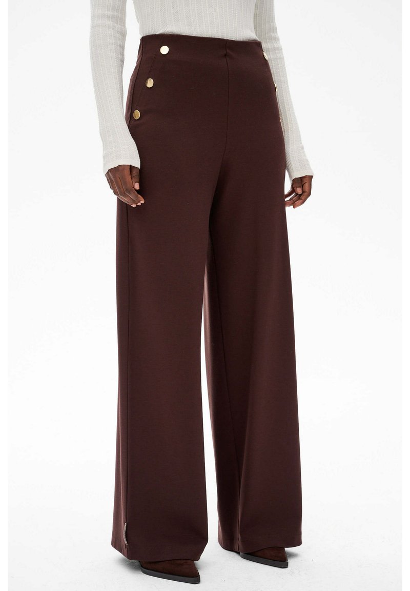 Brązowe spodnie o szerokich nogawkach, wykonane z miękkiego materiału, z wysokim stanem i złotymi guzikami po bokach. Gładka tekstura i dopasowany krój.