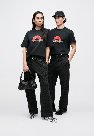 T-shirts pretas com um logótipo, calças pretas com padrão, uma mala preta texturada e sapatos prateados brilhantes. Figuras estão lado a lado.