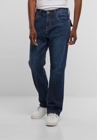 Temno modri kavbojke iz denima s ravnim krojem, petimi žepi, kontrastnim rumenim šivom in gumbom za zapiranje v pasu.