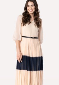 Abito maxi plissettato in pesca con un effetto dip-dye blu navy sul fondo, maniche a palloncino trasparenti e una cintura nera in vita.