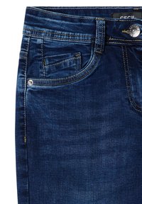 Gros plan sur un jean en denim bleu foncé montrant une poche avant, une petite poche à monnaie, des passants de ceinture, un bouton avec détails de couture sur fond blanc.