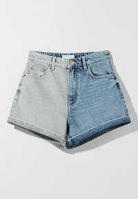 Farkkushortsit, joissa väri-blokkisuunnittelu: vasemmalla vaaleanharmaa ja oikealla tummansininen. Käännetyt lahkeet ja vakio viiden taskun malli.