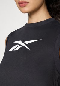 Crna majica bez rukava s istaknutim bijelim Reebok logotipom. Izrađena od glatkog, rastezljivog materijala s okruglim izrezom i bez vidljivih šavova.