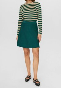 Raidallinen pitkähihaine paita beigen ja tummanvihreän s�ävyissä, yhdistettynä mintunvihreään A-linjaisiin hameeseen. Mallilla on päällä mustat kengät, joissa on niittidetaljeja.