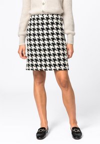 Houndstooth-kuvioinen hame mustavalkoisena, polvipituinen, valmistettu teksturoidusta kankaasta. Yhdistetty mustiin loafereihin ja vaaleaan neuleeseen.