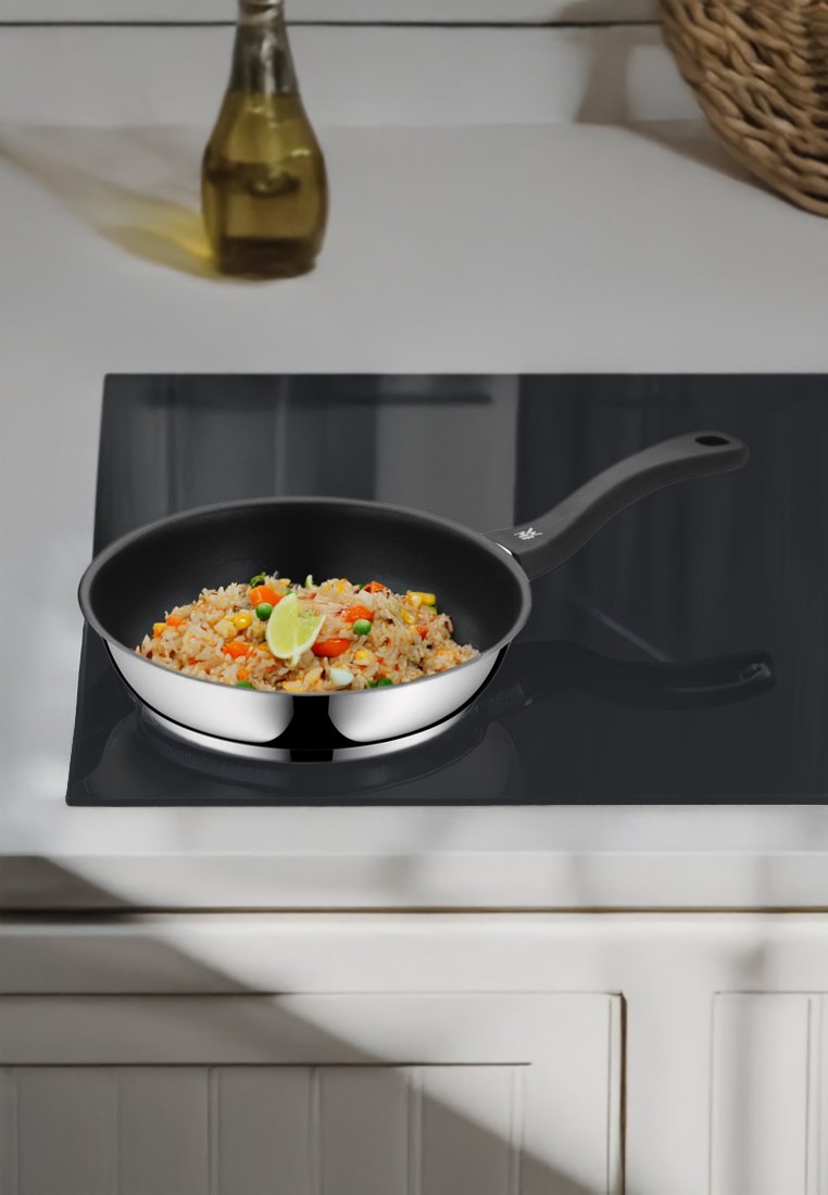 Sartén antiadherente con un mango negro, llena de arroz frito colorido y una rodaja de lima, colocada sobre una estufa negra brillante.