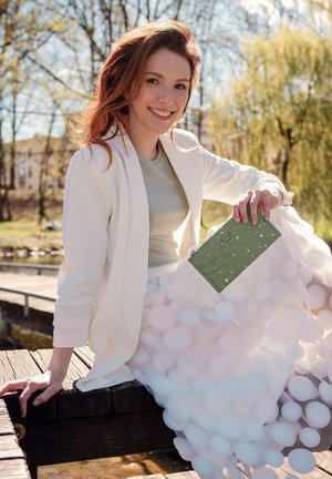 White blazer over a light green shirt, paired with a textured, circular-patterned, white skirt. Holding a light green clutch with a design.