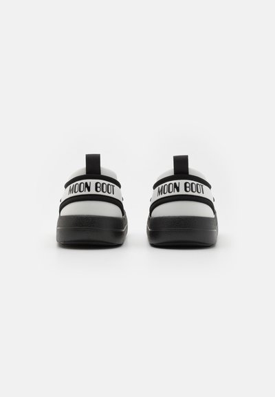 Cizme MOON BOOT alb-negru, cu o talpă groasă neagră, având curele duble negre și bucle la spate pentru o îmbrăcare ușoară.
