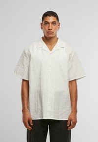 Camicia bianca a maniche corte con un motivo testurizzato, dotata di colletto, bottoni sulla parte anteriore e una vestibilità rilassata.