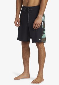 Zwarte zwemshorts voor mannen met een camouflage zijpaneel in groen, bruin en beige. Sneldrogend materiaal met een verstelbare trekkoord taille.
