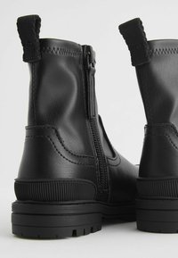 Bottes chevilles en cuir noir avec fermeture éclair sur le côté, finition texturée, languette de tirage et semelle en caoutchouc durable avec accents striés.