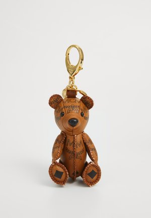 Porte-clés en cuir marron en forme d'ours en peluche avec des motifs de logo noirs, des détails cousus et un fermoir doré sur fond blanc.