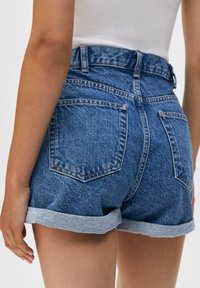 Jeansshorts i mellanblått med hög midja, uppvikta fållar och två bakfickor med kontrasterande sömnad.