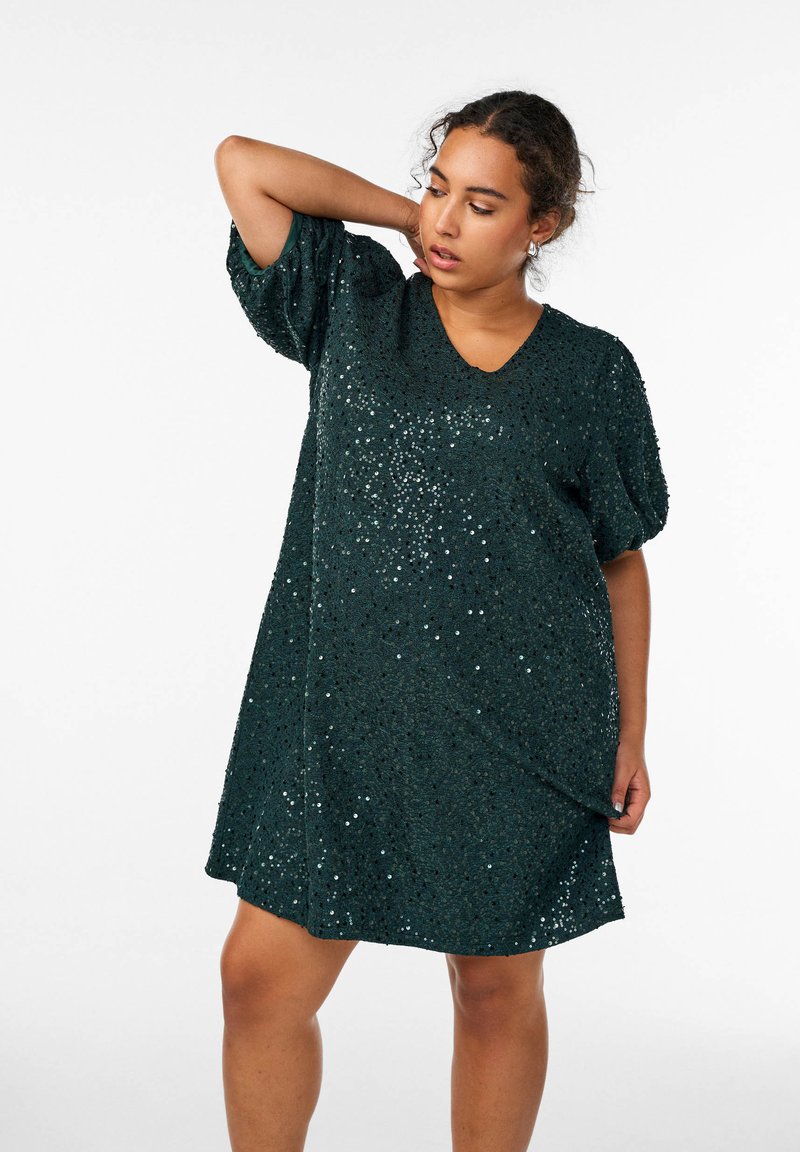 Abito verde con paillettes, scollatura a V e maniche a palloncino corte. Il tessuto presenta una superficie testurizzata decorata con paillettes luccicanti.