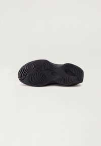 Semelle de basket noire avec motif de bande de roulement ondulé et texturé conçu pour l'adhérence, montrée sur un fond clair uni.