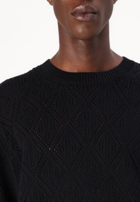 Sort strikket sweater med et tekstureret diamantmønster, rund crew neckline og ribbede ærmer. Materialet virker blødt med en let glans.