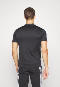 Camisa polo negra con un diseño ajustado, mangas cortas y acentos azules en los hombros. Fabricada con tela lisa y elástica para mayor comodidad y flexibilidad.