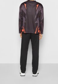 Svart atletisk jacka med orange accenter, med ett modernt geometriskt mönster och avslappnad passform, i kombination med matchande svarta byxor.