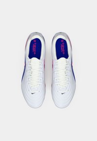 Λευκά ποδοσφαιρικά παπούτσια με υφασμένο πάτο, μοβ και ροζ λεπτομέρειες, επίπεδοι κορδόνια και λογότυπο της Nike στο πλάι και στη γλώσσα.