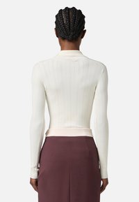 Top bianco a maniche lunghe con una silhouette aderente e una fascia in contrasto di colore chiaro in vita. La vista posteriore mostra un design minimalista.