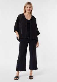 Czarna, lekka, teksturowana koszula z zapięciem na guziki, w połączeniu z czarnym topem na ramiączkach i szerokimi spodniami. Uzupełniona klapkami.