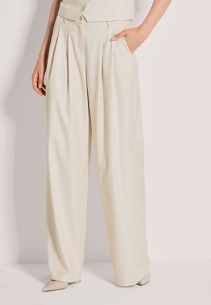 Beige Hosen mit weitem Bein und Falten, aus leichtem Stoff gefertigt. Verfügen über einen hohen Bund und Seitentaschen. Kombiniert mit hellen spitzen Schuhen.