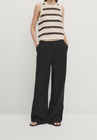 Top a crochet con strisce crema e marrone scuro, abbinato a pantaloni larghi neri. I pantaloni presentano pieghe e una vestibilità rilassata.