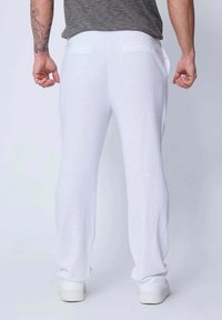 Pantalon en lin blanc avec une coupe décontractée, doté de poches arrière et d'une texture lisse. Porte un t-shirt gris et des baskets blanches.
