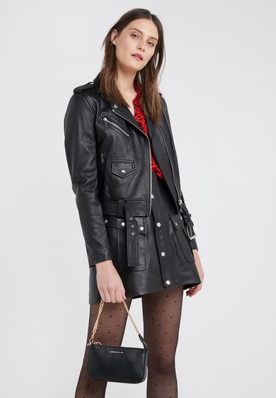 Veste de motard en cuir noir avec poches zippées, matériel en argent, taille ceinturée, et superposée sur un haut à motif rouge et noir.