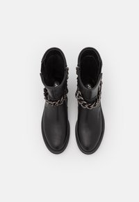 Botas de tobillo de piel negra con un acabado liso, con un acento de cadena alrededor del tobillo. Punta redondeada y suela plana. Cremallera en el lateral.