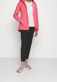 Chaqueta impermeable rosa con capucha, combinada con una camiseta blanca, joggers negros y zapatos rosas, con patrones sutiles y un diseño robusto.