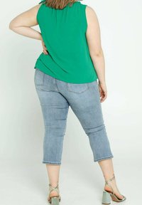 Top verde senza maniche con scollatura arricciata, abbinato a jeans cropped azzurri e sandali con tacco verdi a strisce.