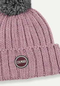Růžová pletená čepice s vroubkovanou texturou a šedým bambulí na vrchu. Obsahuje kulatou nášivku s logem "COLMAR" v bílé barvě na tmavém pozadí.