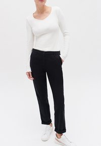 Vit ribbad långärmad topp i kombination med svarta byxor med knäppning och uppvikta ärmar, bärs med vita sneakers.