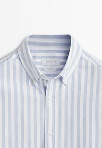 Chemise à col avec des rayures verticales bleu clair et blanches, dotée d'un col boutonné et de boutons blancs.