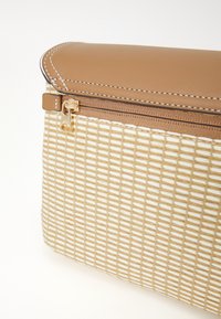 Beige gewebte Stofftasche mit einem oberen Teil aus braunem Synthetikmaterial. Verfügt über einen goldenen Reißverschluss mit einer strukturierten Oberfläche und weißer Naht entlang der Kanten.