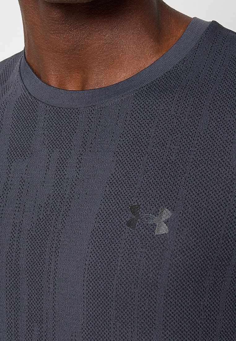 Maglietta sportiva grigia realizzata in tessuto testurizzato e traspirante, con colletto a coste, caratterizzata da un logo Under Armour nero sul davanti.