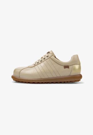 Beige leren vetersneaker met bruine rubberen zool en subtiele stiksel details op een witte achtergrond.