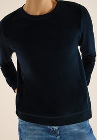 Laivastonsininen collegepaita, jossa on pehmeä, teksturoitu pinta, pyöreä kaula-aukko ja resorit hihansuissa. Suora leikkaus ja hillitty logodetail helmassa.