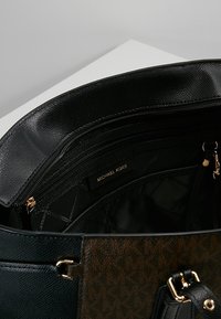 Zwarte en bruine leren tote bag, met ritssluiting vakken, gouden hardware accenten en een gestructureerde buitenkant met een logo voering.