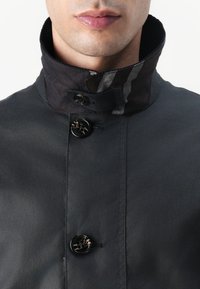 Veste de couleur foncée avec un col montant, dotée d'une doublure rayée et de deux grands boutons pour la fermeture. Texture lisse dans l'ensemble.