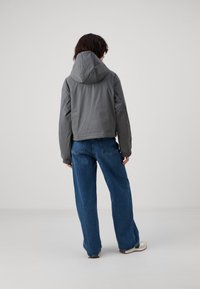 Grå hettejakke med en cropped design, teksturert stoff og elastiske mansjetter, kombinert med løse, blå denimbukser og hvite sko.