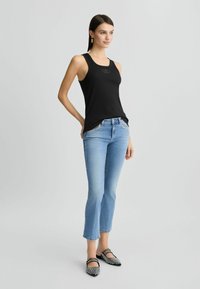 Débardeur noir à côtes avec un col rond, associé à un jean court bleu clair et des chaussures plates à carreaux noir et blanc.