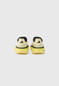 Yellow athletic shoes with a textured fabric upper, black accents, and a thick outsole featuring a zigzag pattern. Rear view showcases design details.