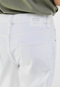 Vaqueros de mezclilla blanca con una textura suave, que cuentan con una etiqueta en el parche trasero y un bolsillo trasero, con un corte ajustado.