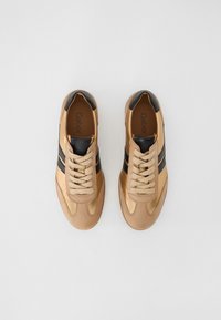 Sneaker color cammello con dettagli neri, caratterizzati da una tomaia in pelle liscia, punta rotonda e chiusura con lacci. Due strisce nere sui lati.