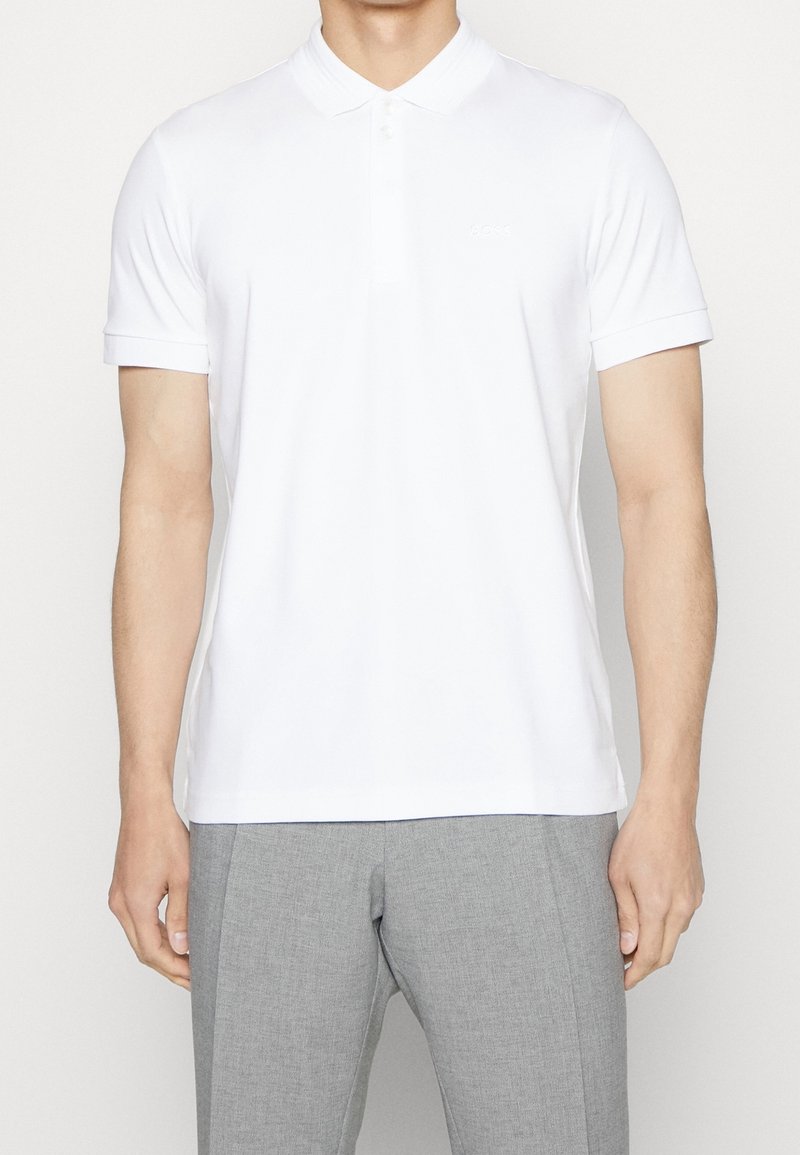Vit polo t-shirt med platt krage, korta ärmar och en diskret logotyp. Tillverkad av slätt tyg, har den en klassisk passform och sidsprund.