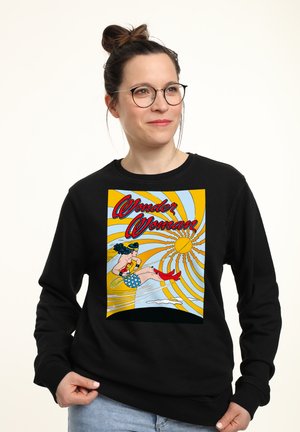Schwarzer Sweatshirt mit einem bunten Wonder Woman-Graphic. Das Design beinhaltet einen leuchtend gelben Hintergrund mit stilisierten Linien und Motiven.