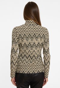 Beige und schwarzer Blazer mit Zickzackmuster, der über einen hohen Kragen und lange Ärmel verfügt, aus strukturiertem Stoff und in taillierter Silhouette.