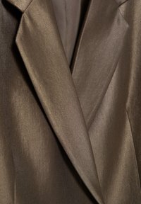 Gros plan sur les revers lisses d'une veste de costume marron montrant la texture du tissu et les détails des coutures.